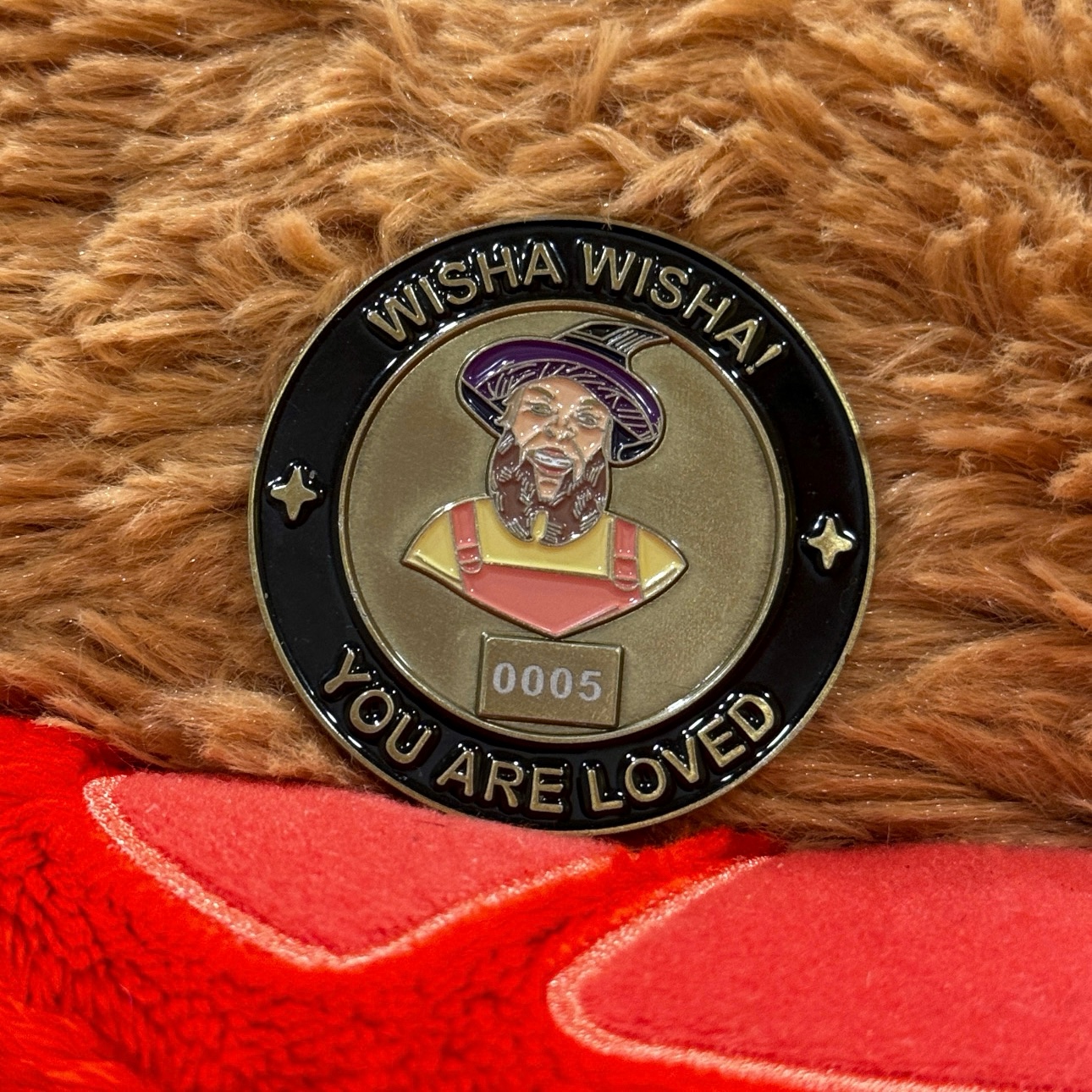 Side A of the wizard coin on a fuzzy brown blanket, showing Gilly's portrait, WISHA WISHA! and YOU ARE LOVED.