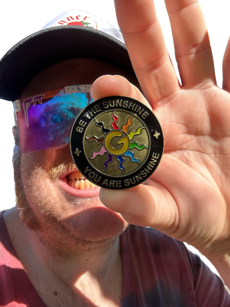 Gilly smiling and holding up the Be The Sunshine wizard coin toward the camera.